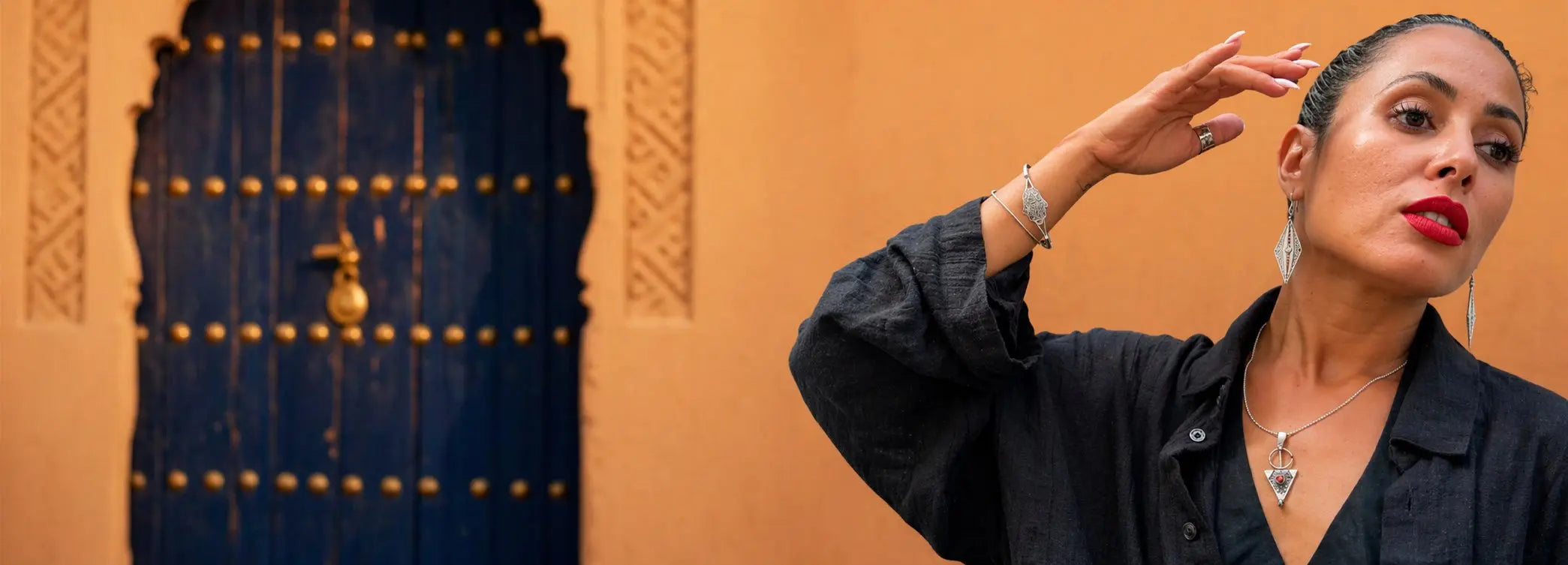 Femme portant des bijoux amazigh devant une porte bleue, format bannière